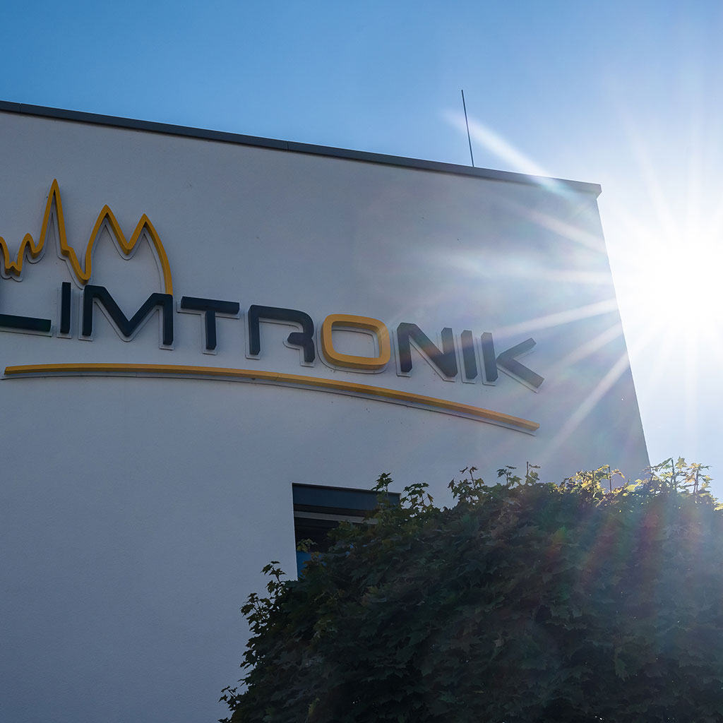 Sonne scheint hinter dem Firmenlogo von Limtronik hervor, umrahmt von Baumkronen