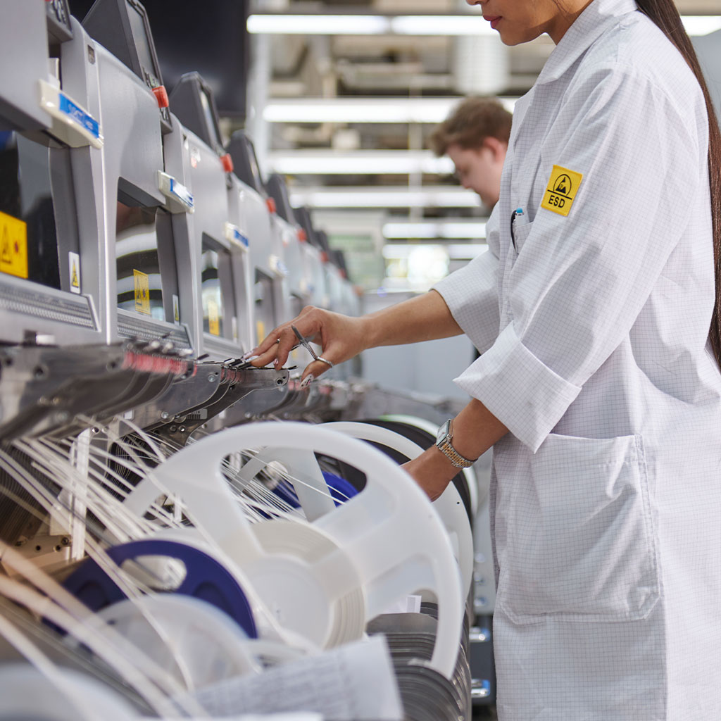 Frau in ESD-Schutzkleidung arbeitet an moderner Bestückungsmaschine in der Elektronikfertigung